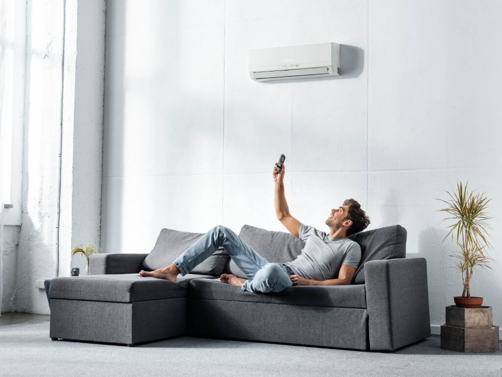 Man lying on sofa and switching on air conditioner